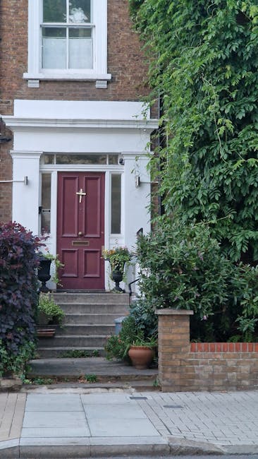A front garden entrance featuring a classic red-painted wooden door with a brass letterbox and handle, situated beneath a white decorative lintel with intricate detailing. The doorstep is accessed via